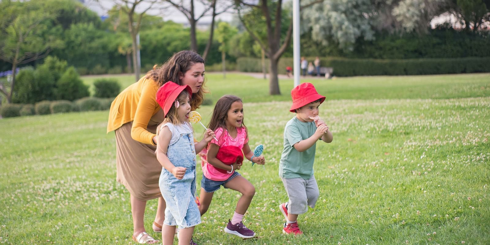 A woman and three children eagerly preparing to run in a grassy park, enjoying a playful outdoor activity.