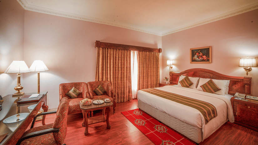 A warmly lit bedroom at Raj Park Hotel - Chennai featuring a plush bed by the window and a sitting area at its foot