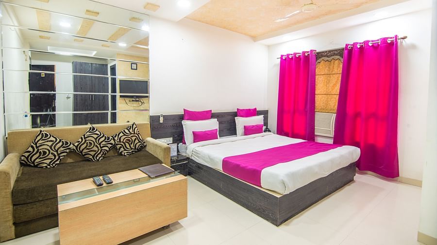A room with a sofa bed, decorative pillows, a coffee table and violet curtains -  Hotel Morya, Bhopal