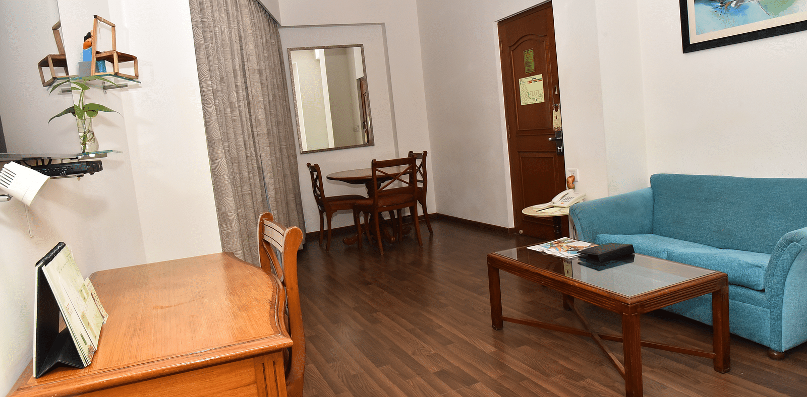 A living area in our suites in Kanchipuram featuring a blue couch and a desk with a chair - Regency Kanchipuram by GRT Hotels