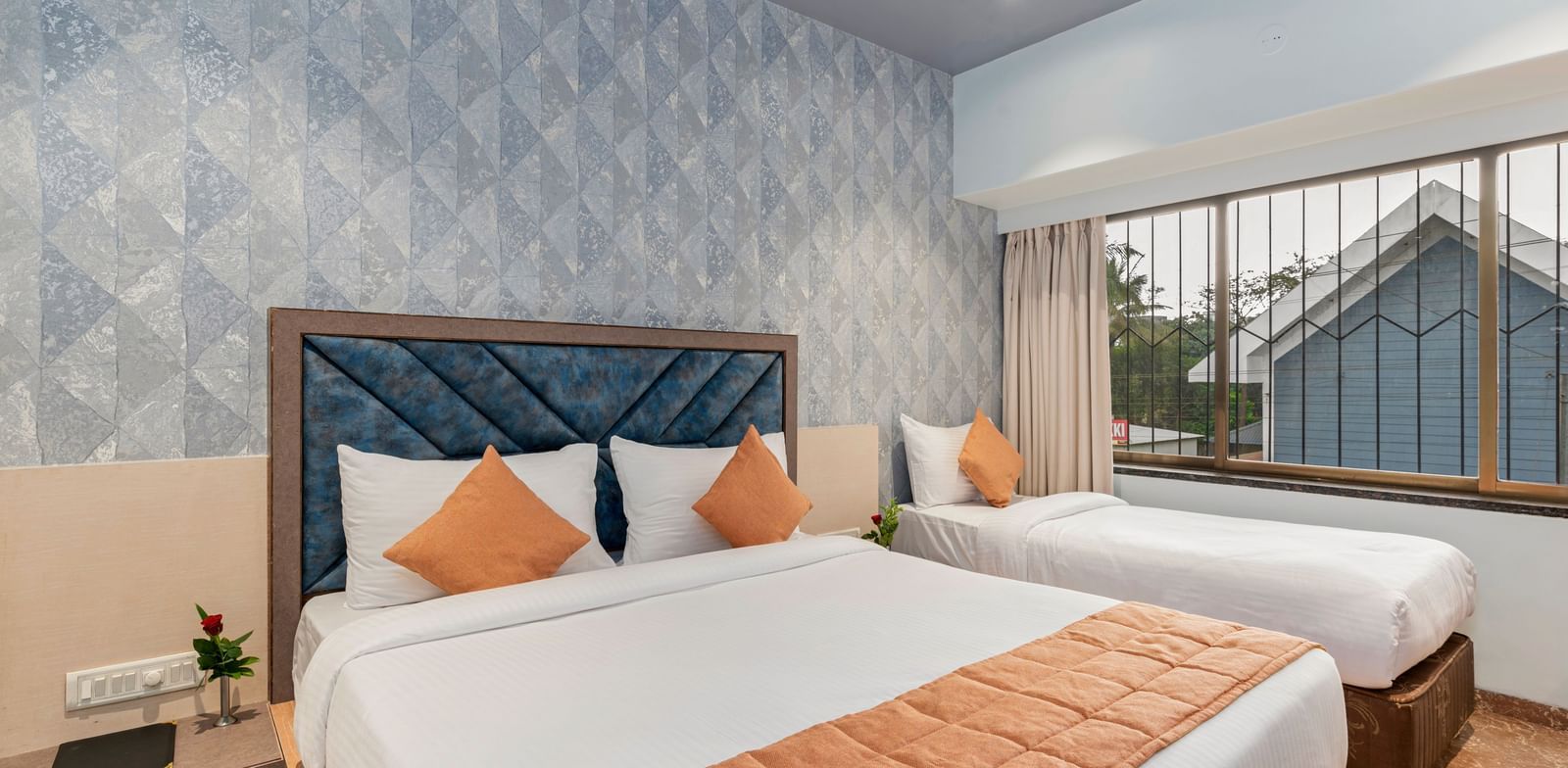 Double bed and a single bed setup at Emerald Retreat, Tungarli with a soft blue accent wall, large windows, and ample natural light.