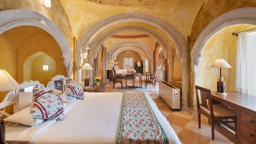 A room with a bed, a desk, a chair, and multiple arched doorways leading to other rooms in Tijara Fort-Palace - 19th Century, Alwar.
