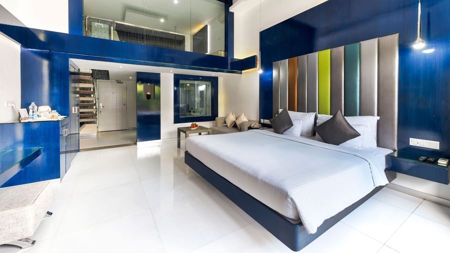 A spacious hotel room with a large bed featuring a blue headboard, a sitting area with a sofa, and a separate raised section that appears to be another sleeping or lounging area, all with dark blue and white decor | Grande Duplex | Grand Bay Resort and Spa