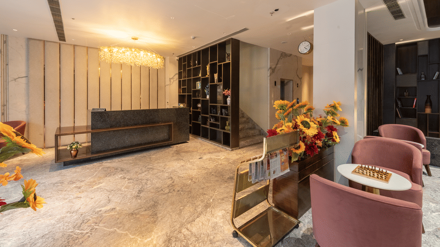A lobby area with 2 chairs, reception desk, tables, and magazine stand arranged indoors at DLS Hotels Amritsar.