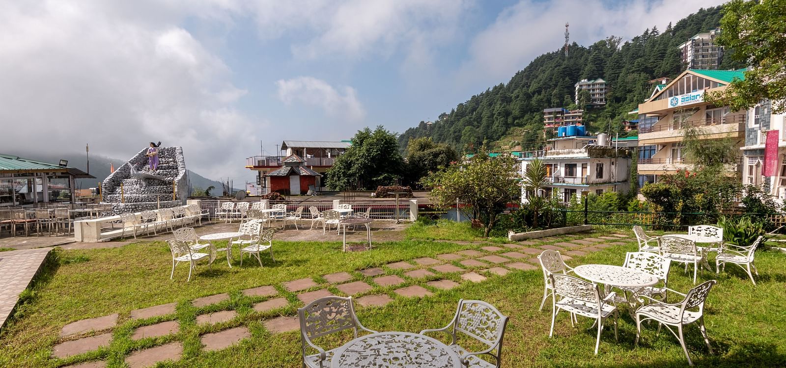 Outdoor seating area with tables and chairs on a lawn overlooking a mountain view - DLS Meghavan Resort