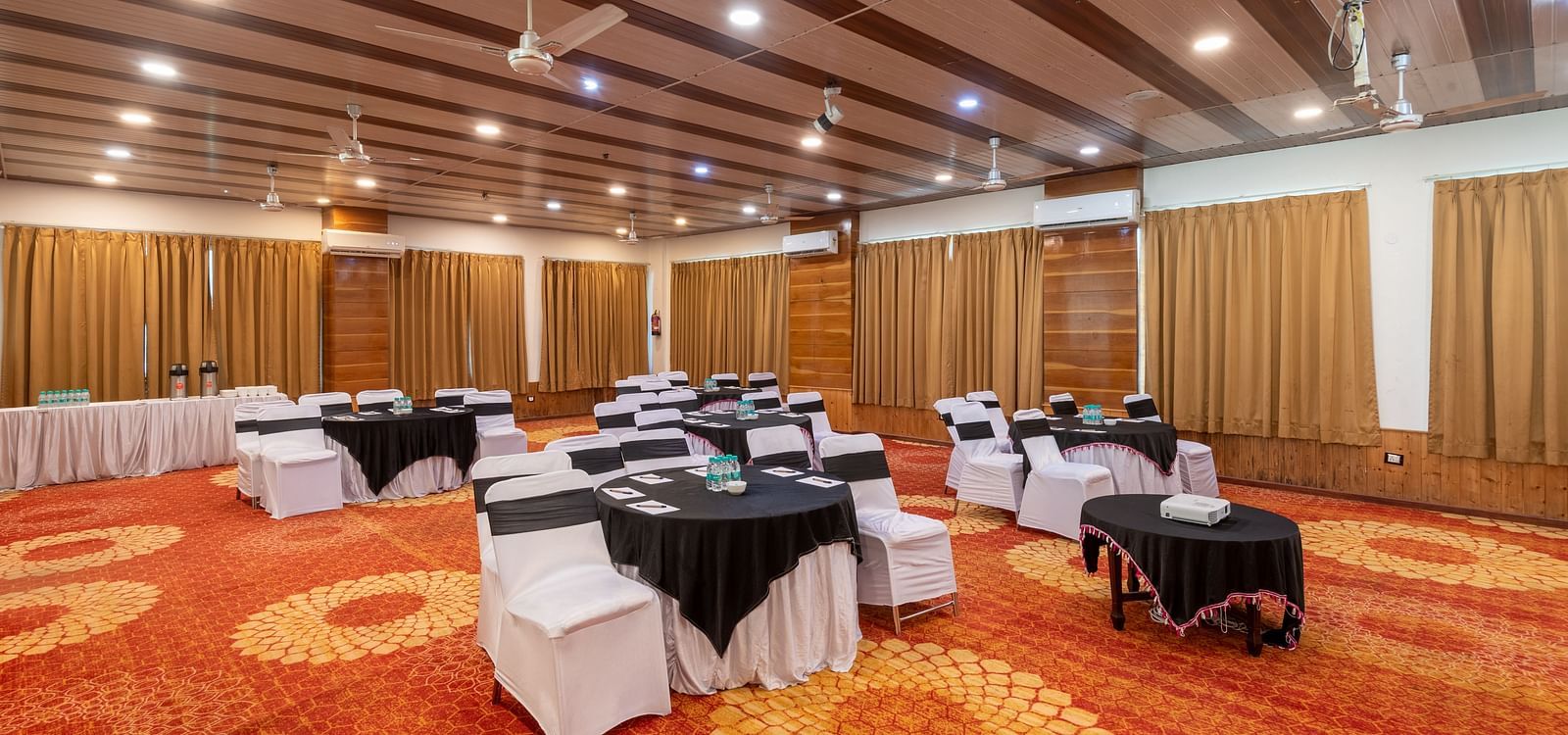 Bright banquet hall with orange carpet, tables and chairs.