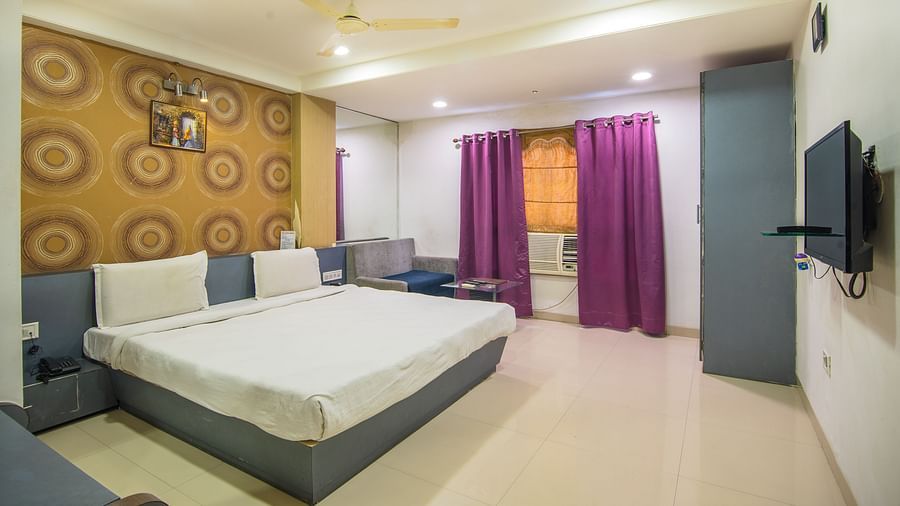 A room with a wall paper sofa, a bed, a TV, an a/c and vibrant curtains - Hotel Morya, Bhopal