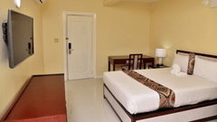 Standard Room at Hotel Grand A View featuring a plush bed facing the TV mounted on the wall over a running table and a work desk with a chair placed by the door