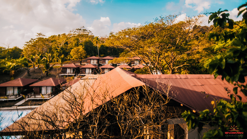 Exterior shot of Symphony Samudra Beachside Jungle Resort And Spa, a 5-star resort in Port Blair, set amidst lush green hills and under a partially cloudy sky.