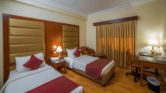 An overview of the twin beds in a inside Deluxe Rooms at Raj Park Hotel, Chennai, featuring a table, a lamp, a study table and a chair. This hotel is one of the best places to stay in Chennai with it's connectivity and convenience.
