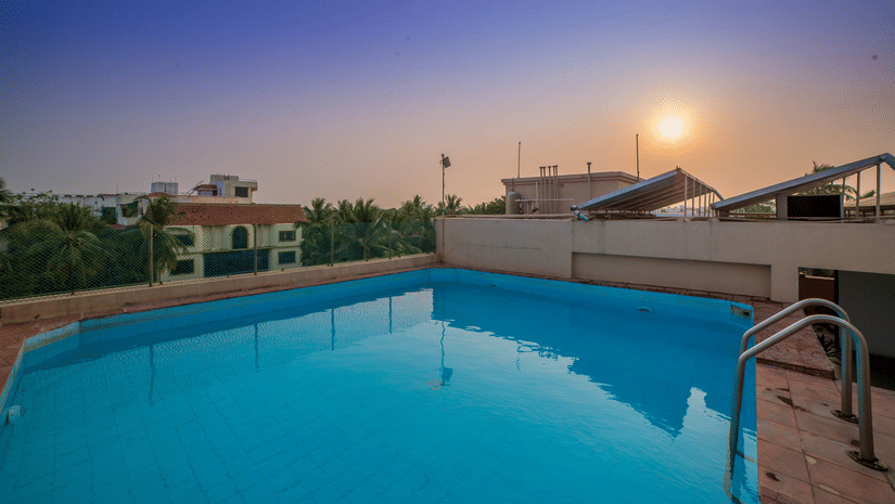 A swimming pool with the sun setting in the background at Raj Park Hotel in Alwarpet, Chennai.