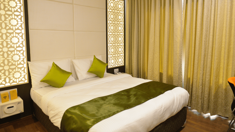 A bed with green runner and pillows beside curtained windows at The Onyx.