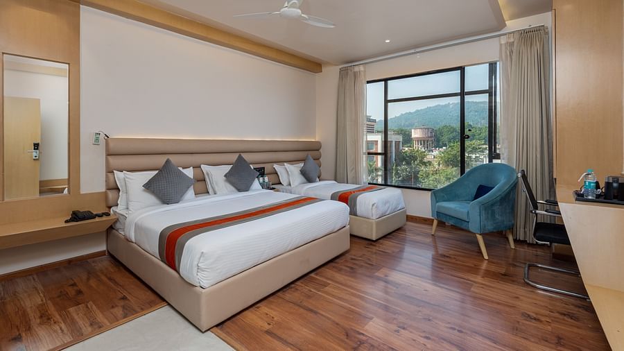 An image of a room with a king size bed and a single bed along with a chair, and a glass window overlooking the city view - DLS Hotel Arihant, Haridwar