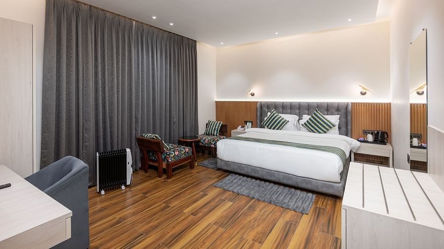 The deluxe room with a bed, chairs, coffee table, and a full length mirror - DLS The Emerald, Nainital