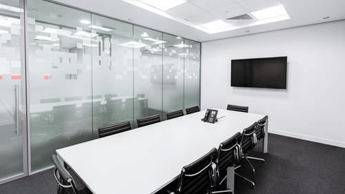 Modern meeting room with glass partitions, long table, and office chairs.