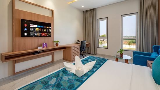 a double bed with blue runner with a tv opposite it inside one of the Rooms - The Orchid Hotel, Jamnagar