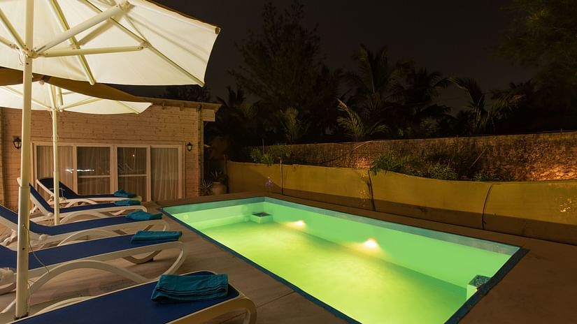 Swimming poolside view at night with pool loungers umbrellas and lightings