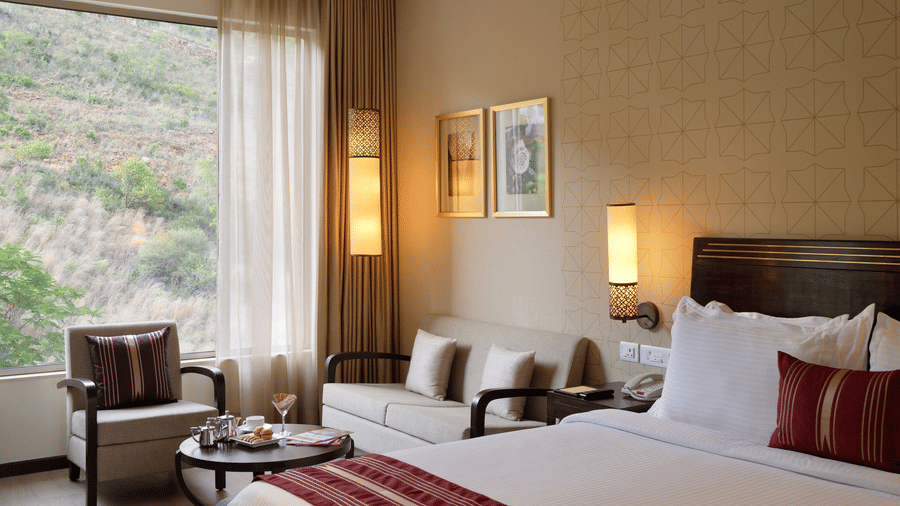 Premium Room at Marasa Sarovar Premiere, Tirupati featuring a king size bed, cosy seating area, large window with scenic hillside views, and warm contemporary interiors.
