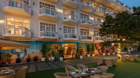 Facade view of DLS Highland Resort and Spa, Mussoorie with comfortable chairs in the lawn at dusk.