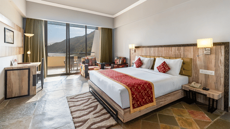 A bed with a runner on it and a large window on one side with a lake view at Via Lakhela Resort & Spa, Kumbhalgarh