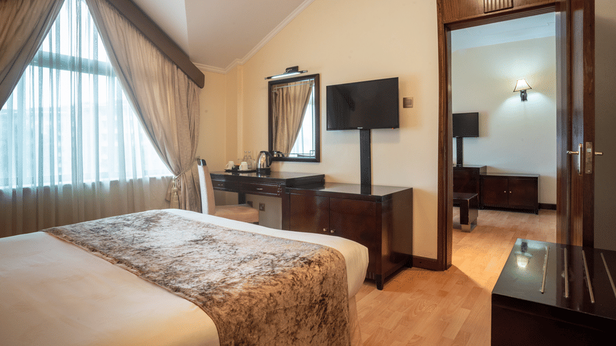 Suite at Boma Inn Nairobi a bed facing a TV on the wall mounted next to the doorway and a mirror on the other side of it near the window