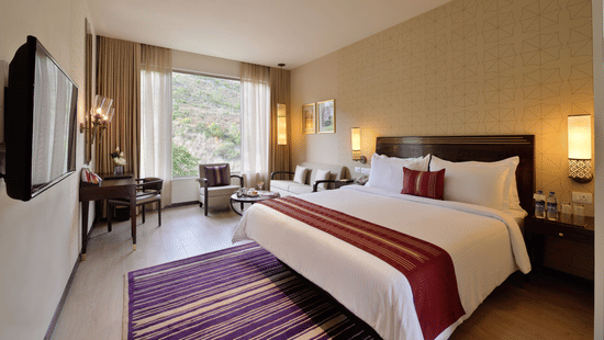 Deluxe Room at Marasa Sarovar Premiere, Tirupati with a king size bed, elegant furnishings, cosy seating corner, and large windows overlooking the surrounding landscape.