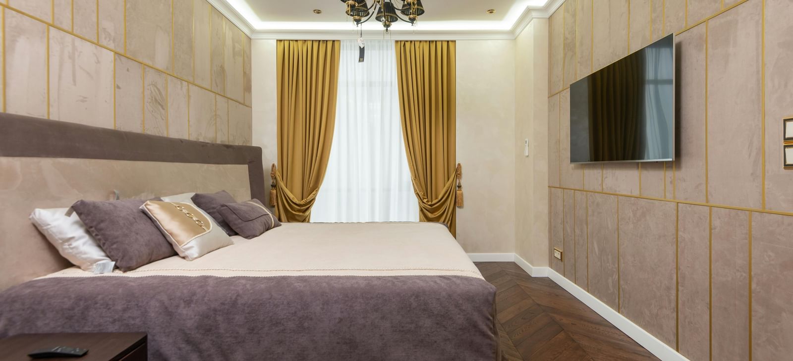 A modern bedroom showcases a large bed, wooden panelling on the walls, and indirect lighting illuminating the space.