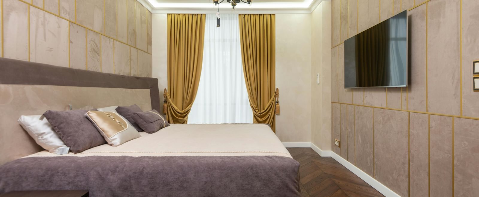 A modern bedroom showcases a large bed, wooden panelling on the walls, and indirect lighting illuminating the space.
