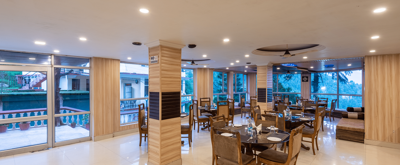 A wide angle shot of a dining area inside the resort featuring tables and chairs | DLS Anupam Resort, Dharamshala