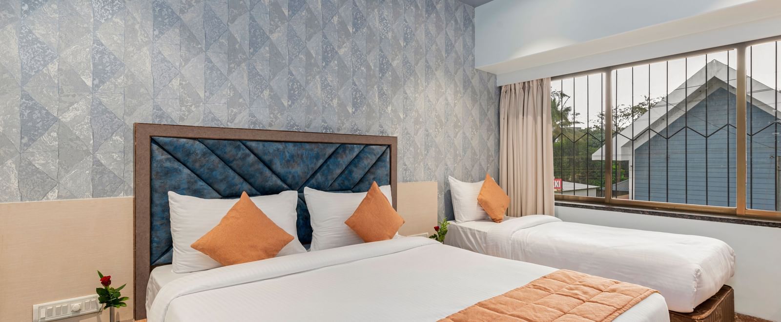 Double bed and a single bed setup at Emerald Retreat, Tungarli with a soft blue accent wall, large windows, and ample natural light.