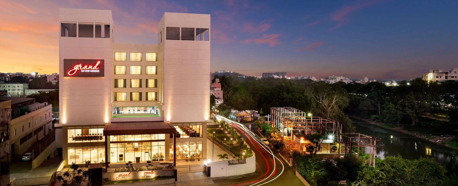 Facade image of Grand Vijayawada by GRT Hotels at night surrounded by green folaige.