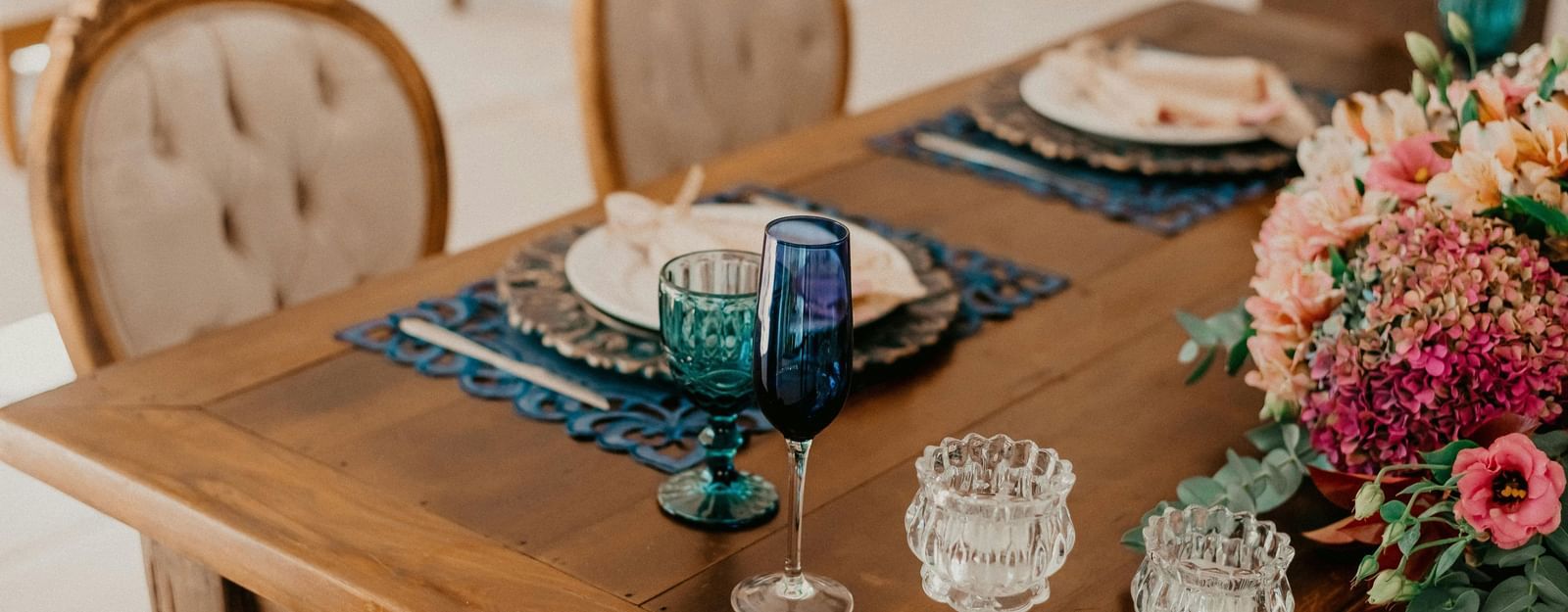 A wooden dining table with dishes arranged neatly on it, featuring floral decorations and cushioned chairs arranged beside it.