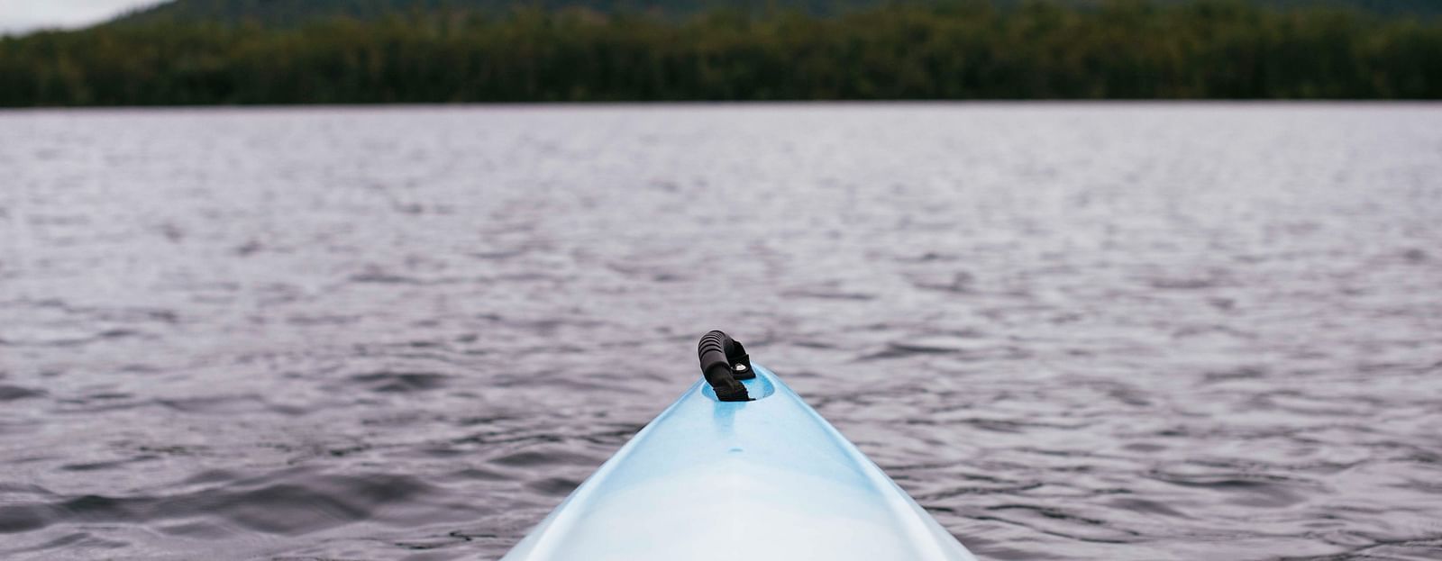 The tip of a kayak in view that is in water with an island in the background