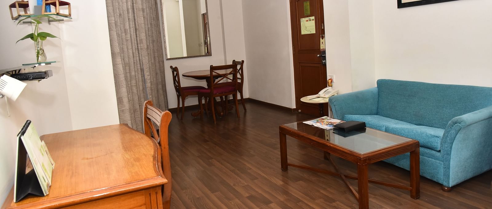A living area in our suites in Kanchipuram featuring a blue couch and a desk with a chair - Regency Kanchipuram by GRT Hotels