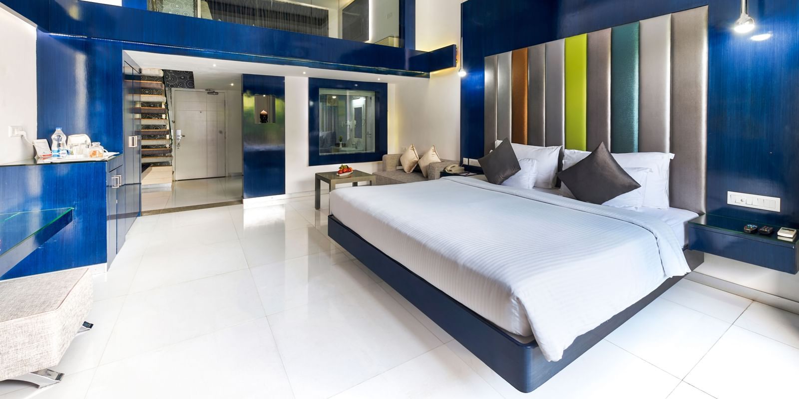 A spacious hotel room with a large bed featuring a blue headboard, a sitting area with a sofa, and a separate raised section that appears to be another sleeping or lounging area, all with dark blue and white decor | Grande Duplex | Grand Bay Resort and Spa