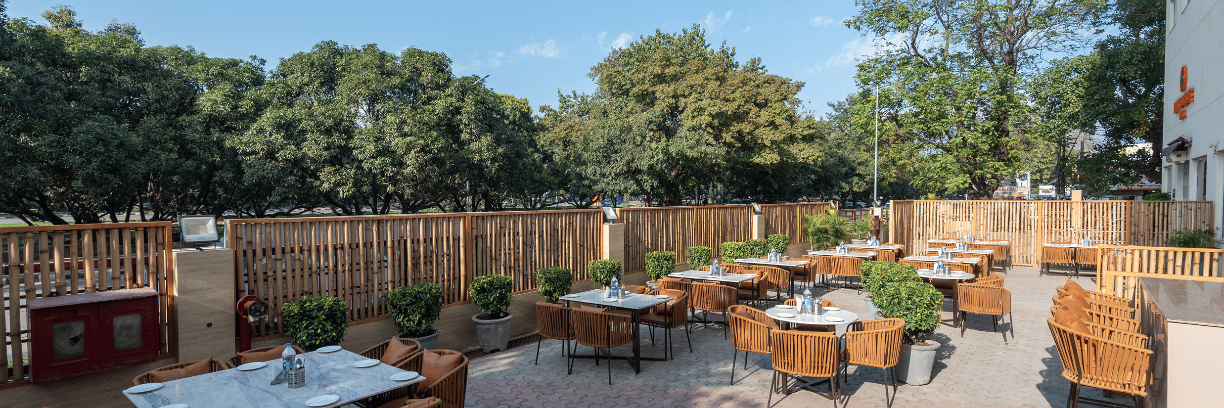 Outdoor seating area with tables and chairs set on a paved patio surrounded by trees at Mango Grove Hotel.