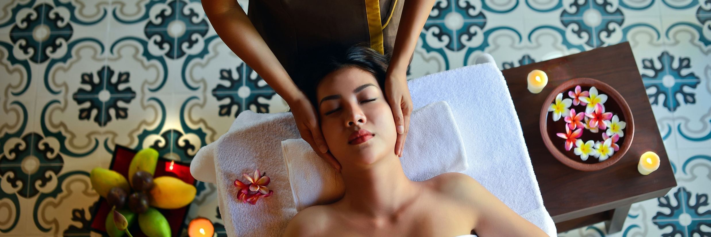 A woman getting a massage from another person with flowers inside a bowl next to her
