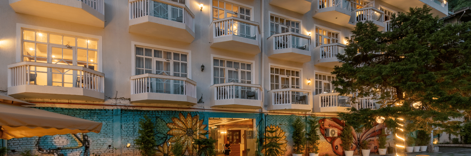 Facade view of DLS Highland Resort and Spa, Mussoorie with comfortable chairs in the lawn at dusk.