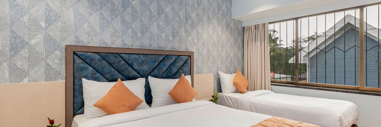 Double bed and a single bed setup at Emerald Retreat, Tungarli with a soft blue accent wall, large windows, and ample natural light.