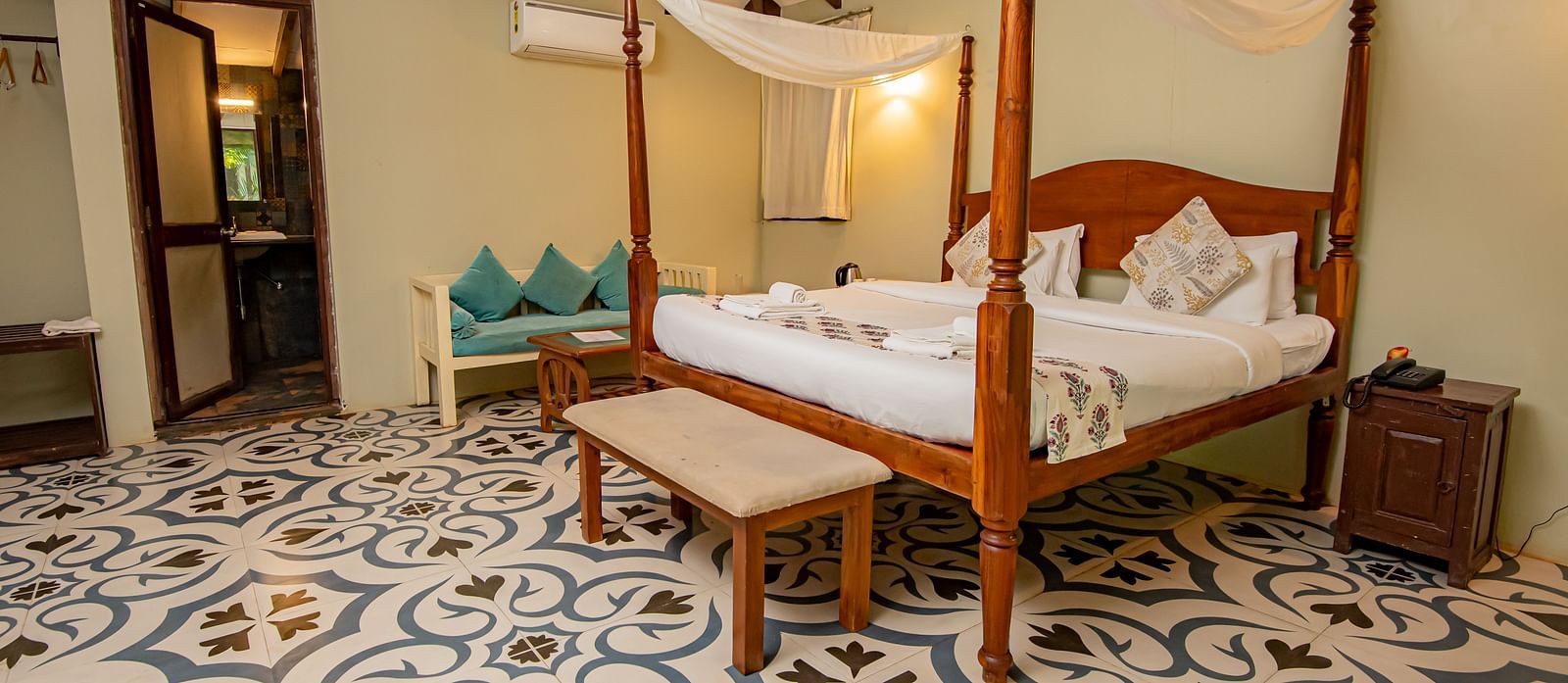 Four-poster canopy bed in a well-lit room with patterned flooring and wooden ceiling beams at De Soul Santé, Morjim.