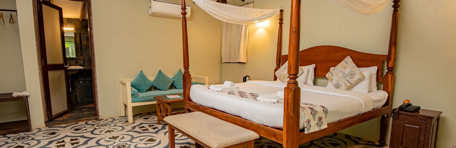 Four-poster canopy bed in a well-lit room with patterned flooring and wooden ceiling beams at De Soul Santé, Morjim.