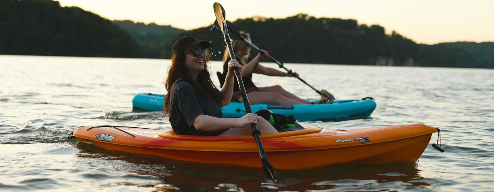 two women kayaking on a waterbody with mountains in the background