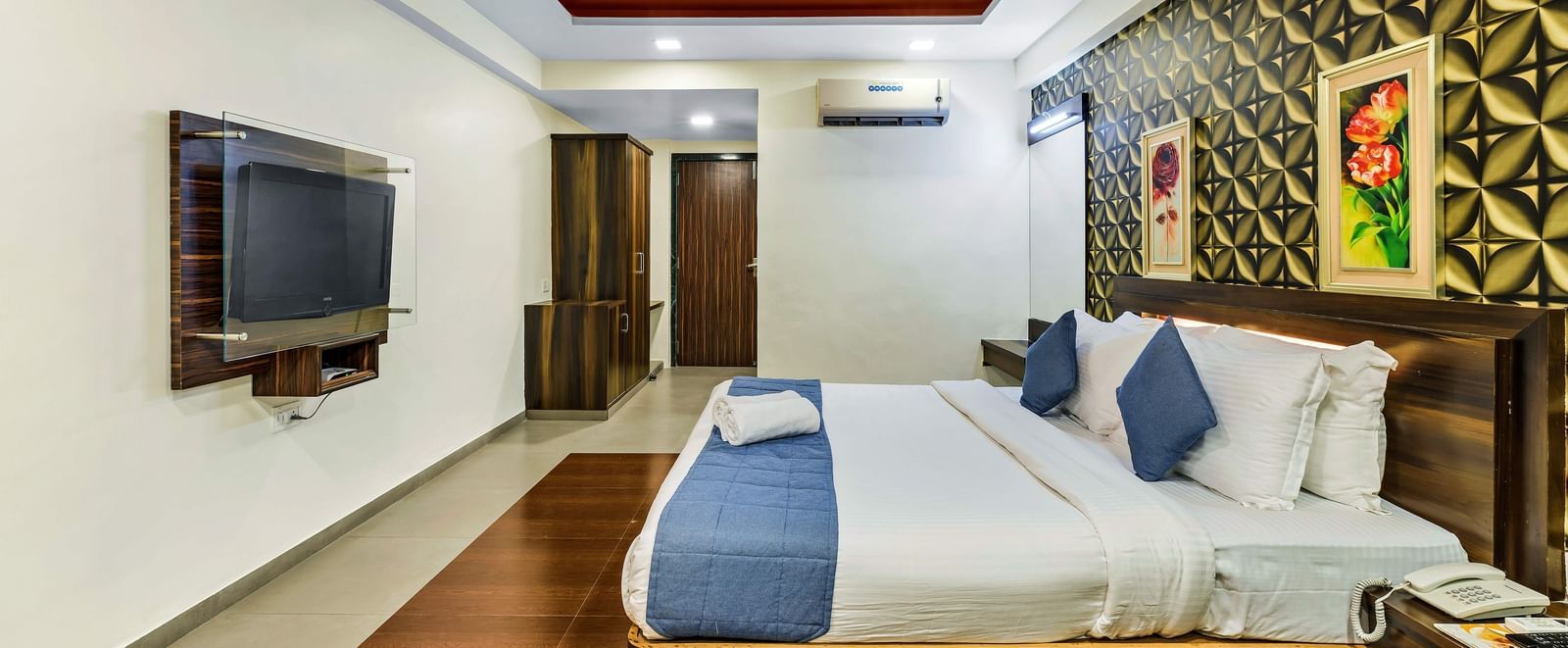 A royal executive room in Krushnai Resort featuring a double bed with blue runner, wall mounted TV and paintings hanging on wall above the headrest.