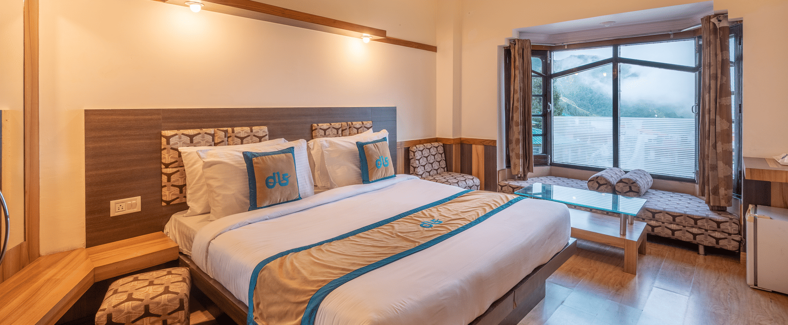 A hotel room featuring a large bed, a window with a mountain view, and a lounge area - DLS Meghavan Resort