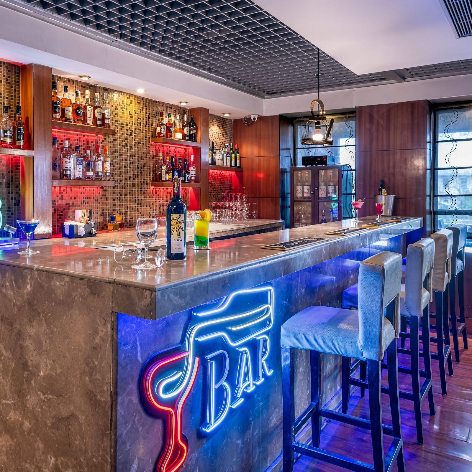 Distil Bar with neon lights, bar chairs, false ceiling, and wooden walls at Lords Plaza Jaipur.