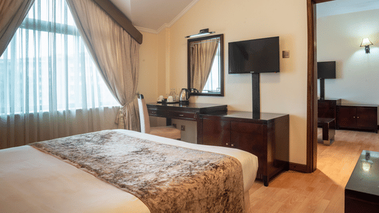 Suite at Boma Inn Nairobi a bed facing a TV on the wall mounted next to the doorway and a mirror on the other side of it near the window