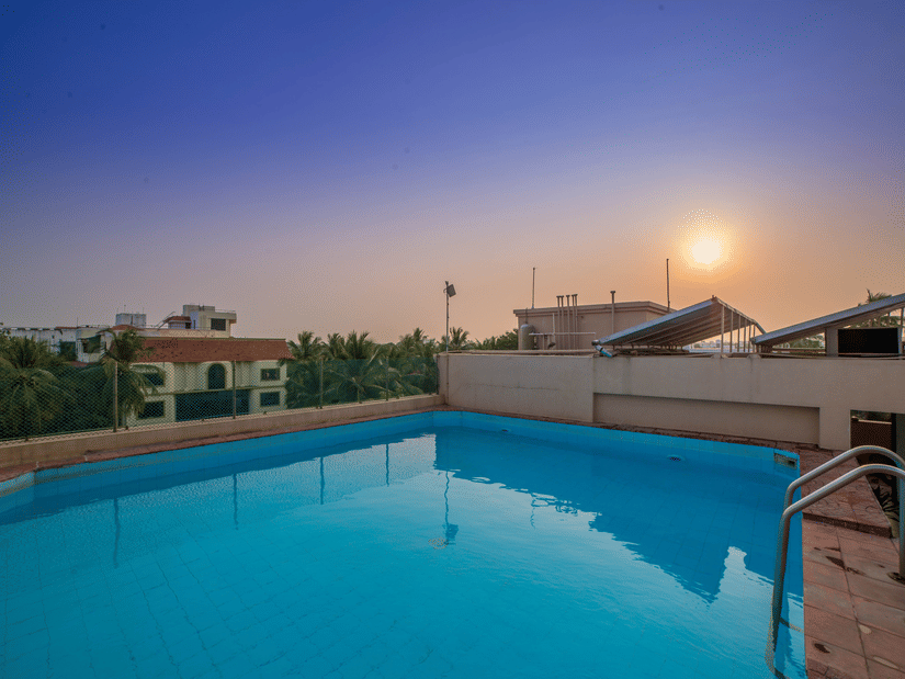 A swimming pool with the sun setting in the background at Raj Park Hotel in Alwarpet, Chennai.