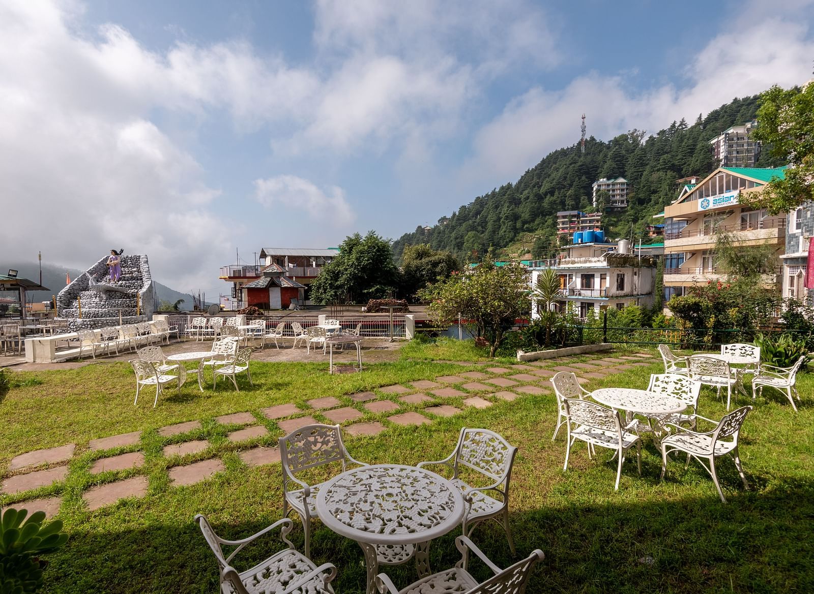 Outdoor seating area with tables and chairs on a lawn overlooking a mountain view - DLS Meghavan Resort
