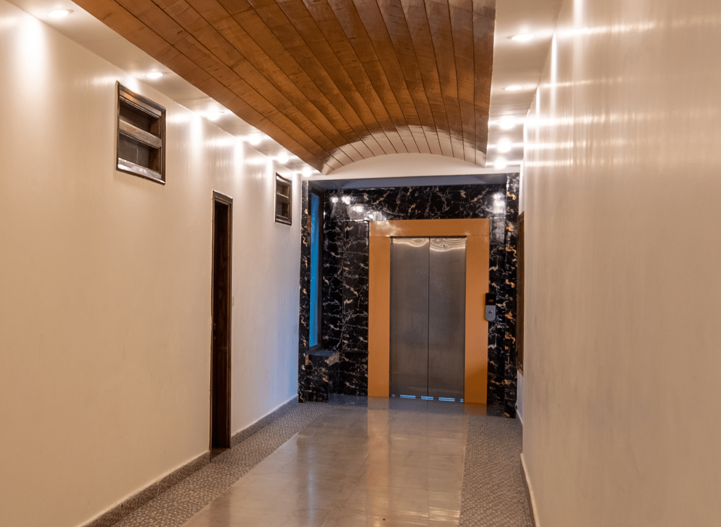 A well-lit hotel hallway with carpeted flooring and guest room doors - DLS Meghavan Resort