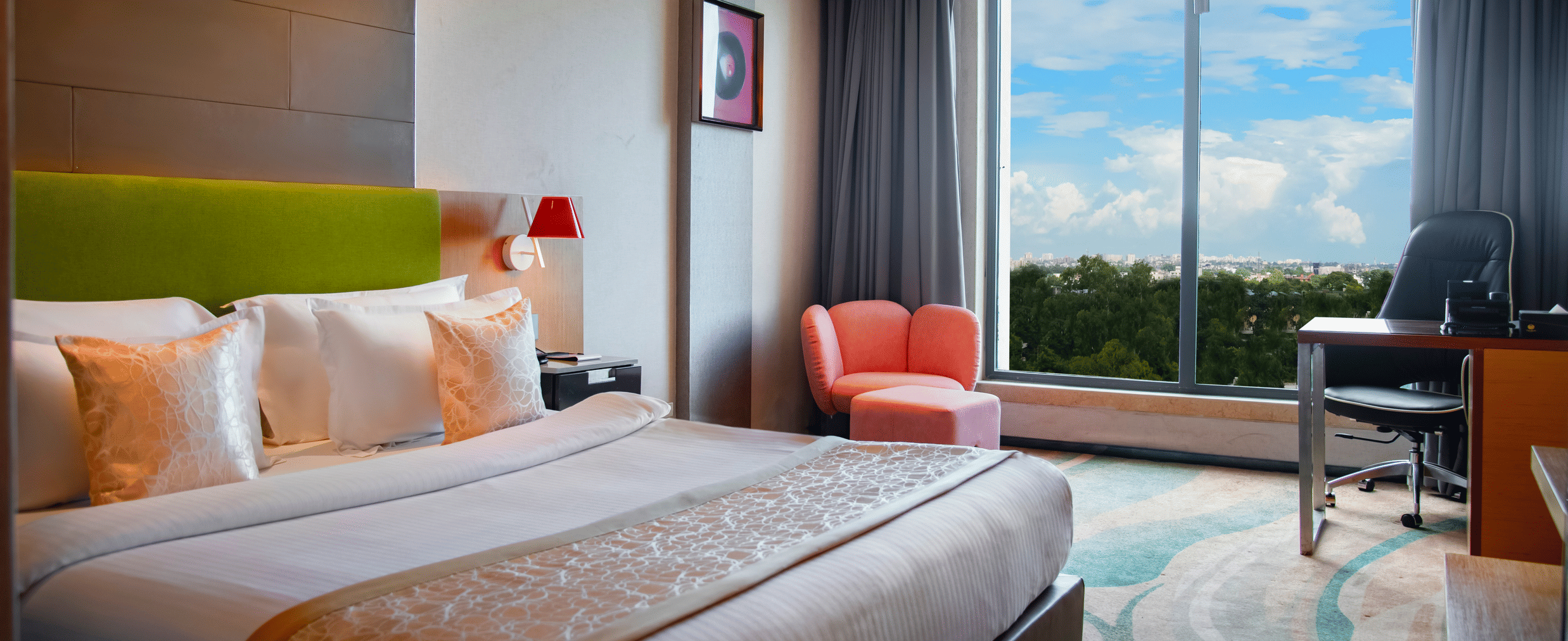 Bedroom at The Regnant featuring double size bed, a sofa,  a work desk and chair, and a large window with view.